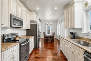 Una cocina con muebles blancos, un refrigerador de acero inoxidable, un microondas y una estufa.