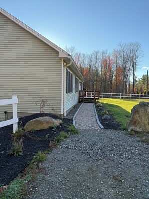 A house with a gravel driveway leading to a wooden deck, surrounded by a white fence and trees with autumn foliage. - Private Berkshire Retreat 9 Acres, Fenced Yard & Dogs Welcome (Otis)