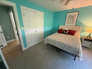 Une chambre à coucher avec un lit, une table de chevet, une porte et un mur orné d’un tableau encadré.