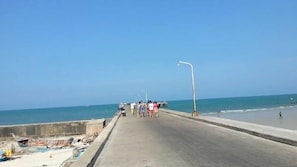 Une route côtière bordée d’une barrière en béton, un ciel dégagé et l’océan en toile de fond.