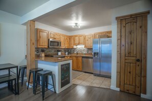 A modern kitchen with wooden cabinets, a stainless steel refrigerator, and a built-in island with bar stools. - Welcome to your beautifully renovated Copper Mountain getaway! (Copper Mountain)