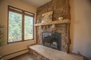 A stone fireplace with a built-in TV, a window with blinds, and a potted plant. - Welcome to your beautifully renovated Copper Mountain getaway! (Copper Mountain)