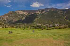 Ein Golfplatz mit einer Bergkulisse, blauem Himmel und einem Wohngebiet im Hintergrund.
