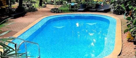 A swimming pool surrounded by lush greenery and a building in the background.