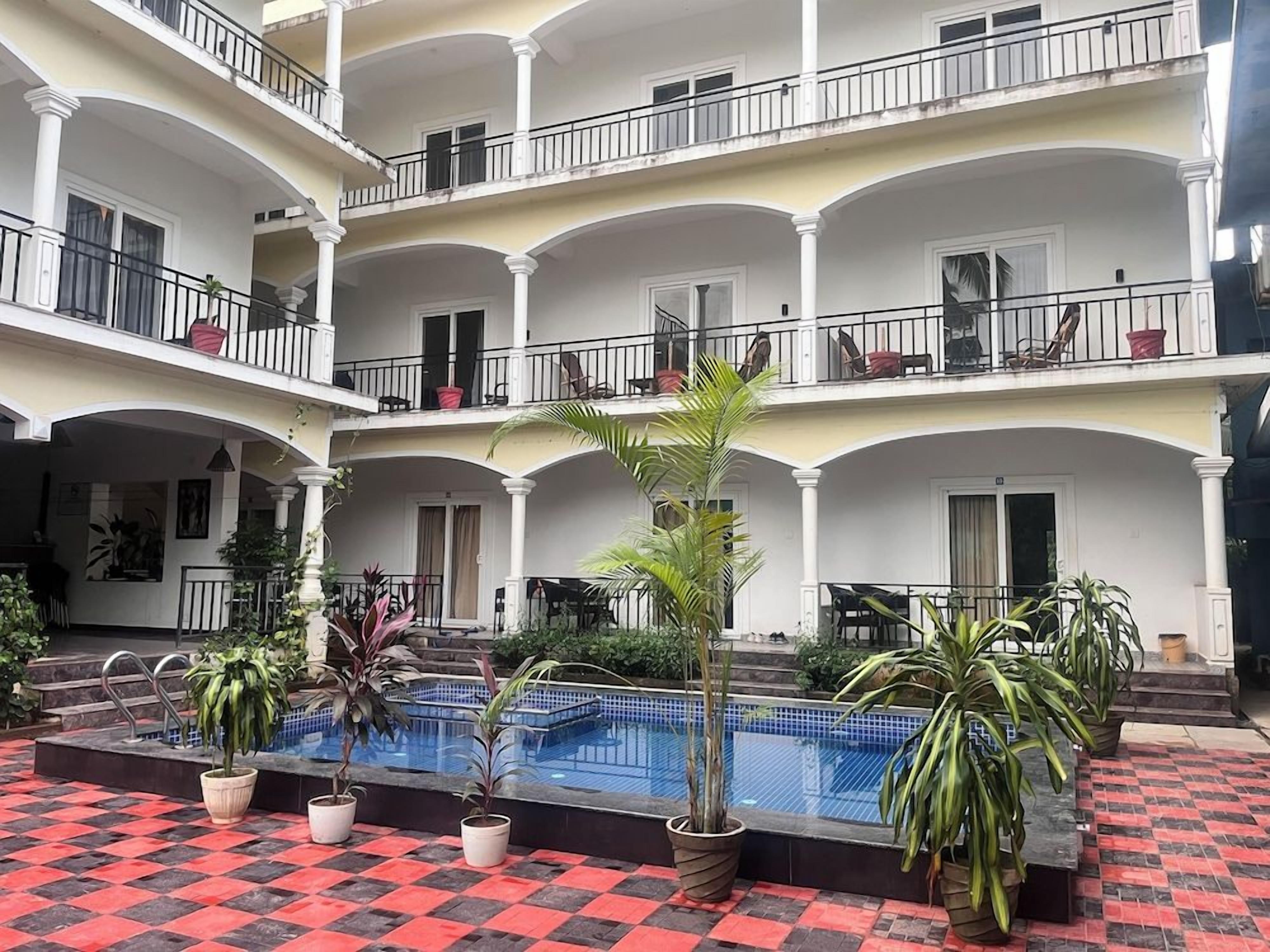 A multi-story hotel with a central pool, balconies, and potted plants.