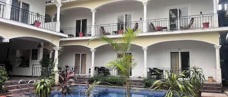 A multi-story hotel with a central pool, balconies, and potted plants.