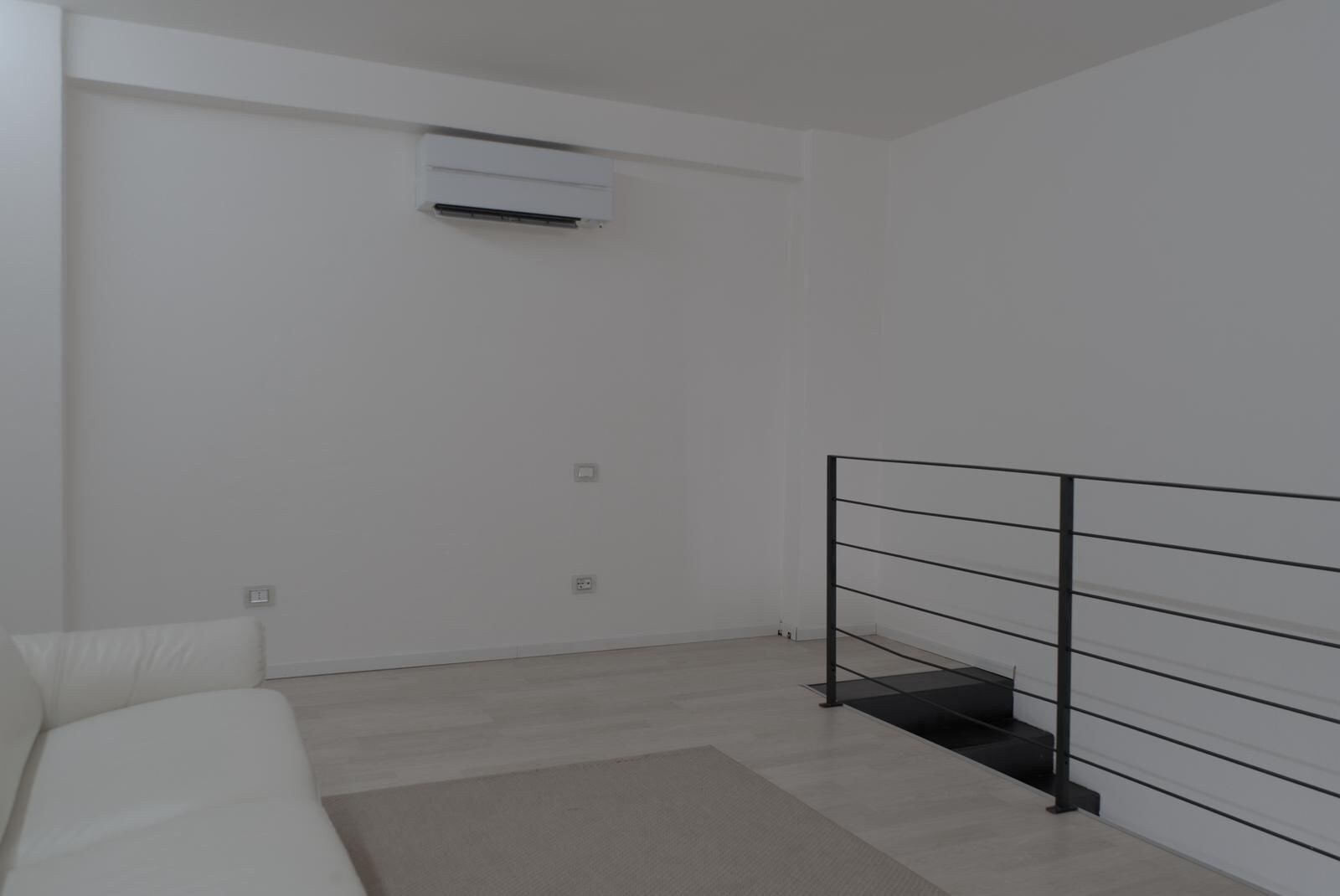 A minimalist room with a white sofa, a black metal railing, and an air conditioning unit on the wall.
