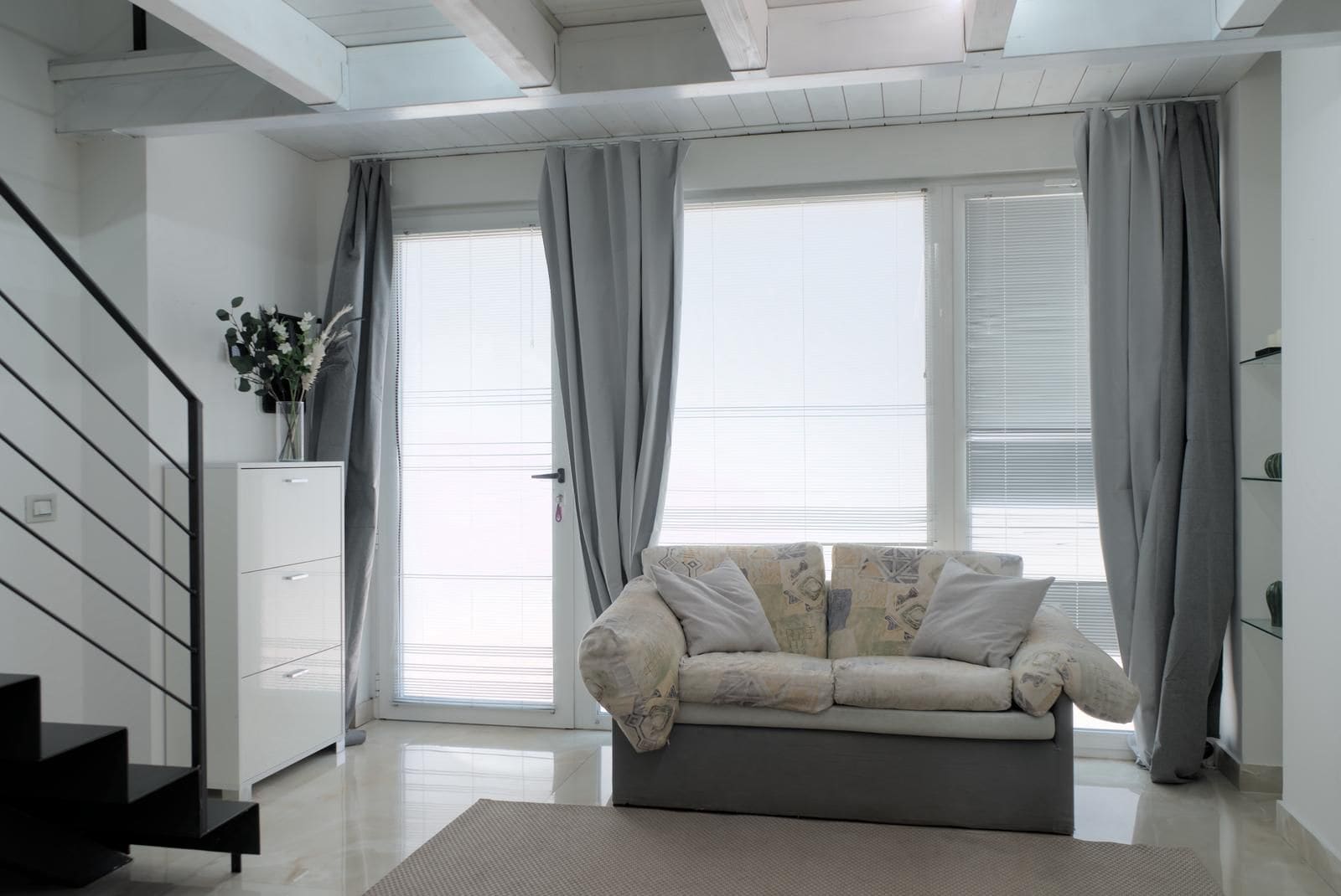 Een moderne woonkamer met een bank, een trap en een raam met gordijnen.