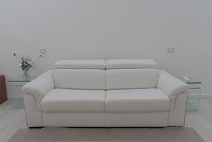 Ein weißes Leder Sofa mit einem Glastisch und einer Blumenvase.