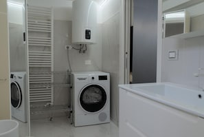 Ein modernes Badezimmer mit integrierter Waschmaschine und Trockner, einer Dusche und einem großen Spiegel.