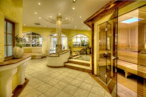 Un área de spa con una fuente de piedra, bancos de madera y una sauna con paredes de vidrio.