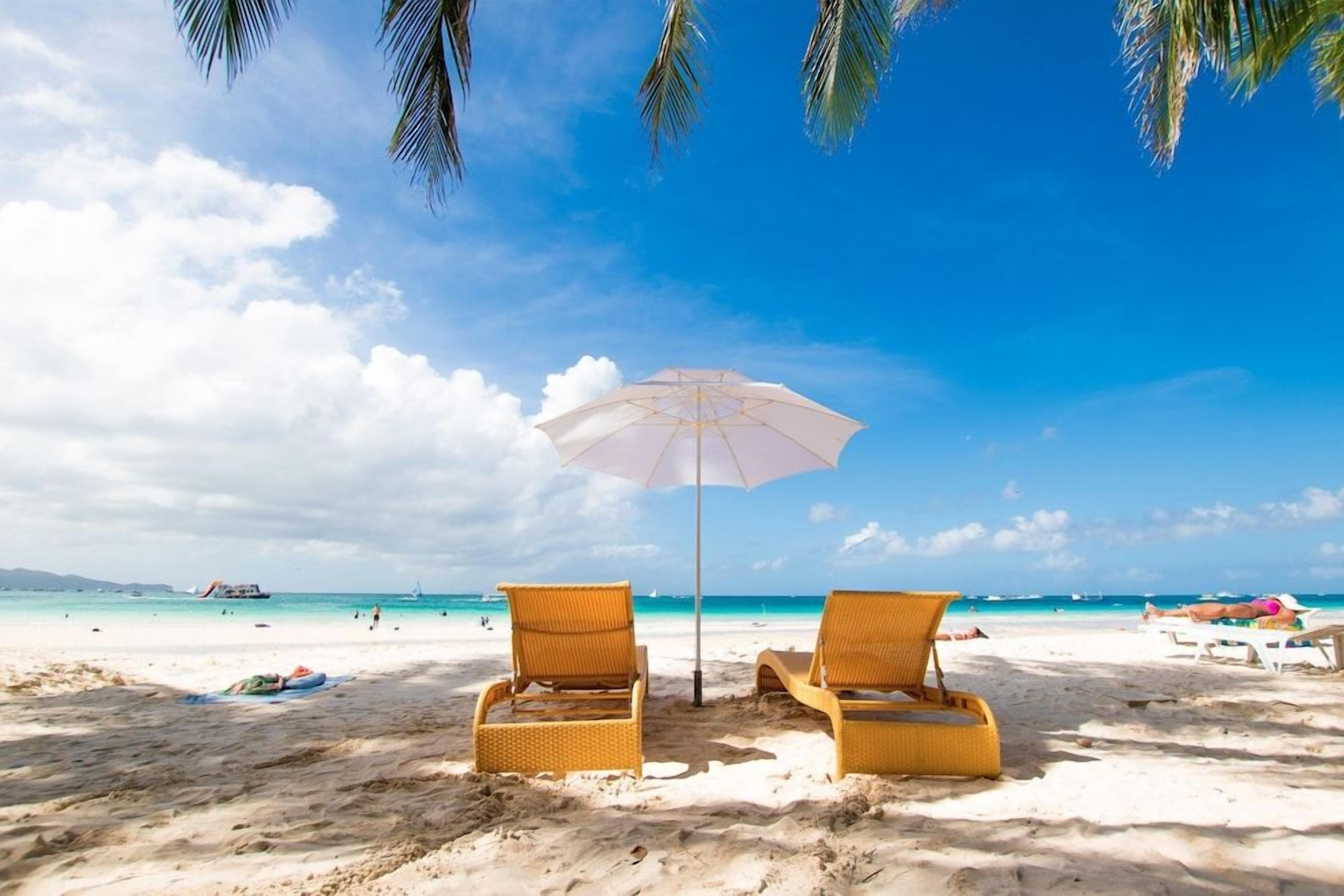 A beach with two wicker lounge chairs and a beach umbrella.