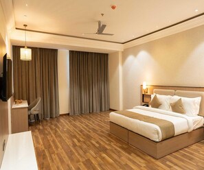 A hotel room with a bed, bedside table, lamp, curtains, and a ceiling fan. - Executive Room Checkin Amritsar (Amritsar)