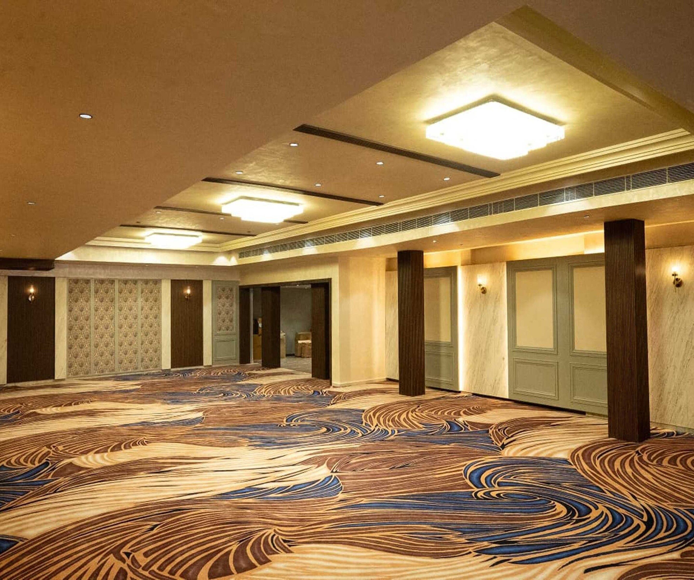 A spacious hall with patterned carpet, recessed lighting, and a high ceiling.
