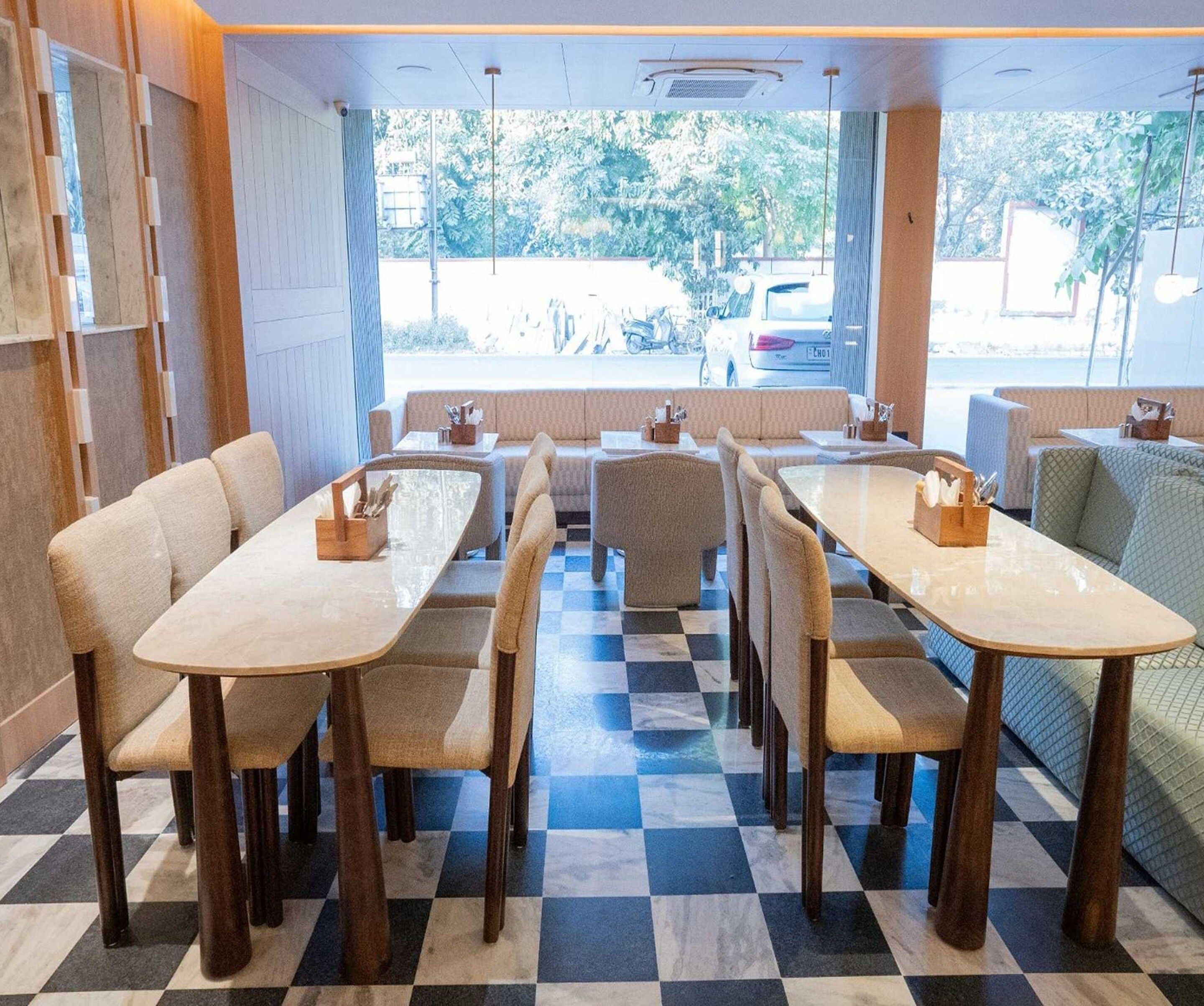 Un restaurant avec un sol à carreaux, de nombreuses tables et chaises, et de grandes fenêtres donnant sur la rue.