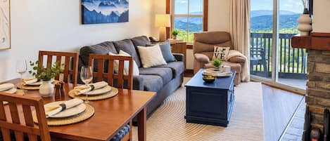 A cozy living room with a dining area, a fireplace, and a scenic view through the windows.