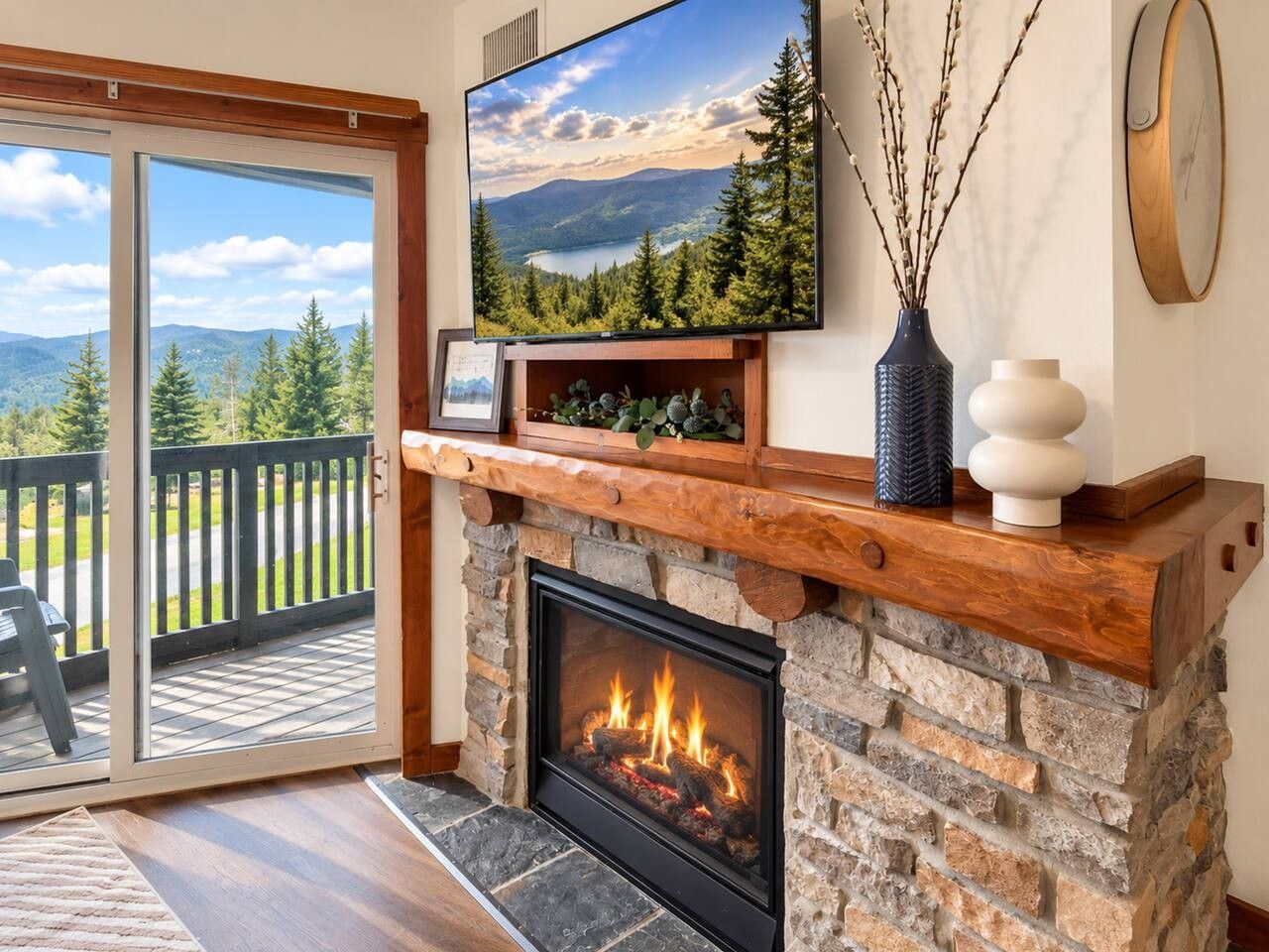 A fireplace with a stone surround, a mounted television above it, and a view of a deck with a wooden railing.
