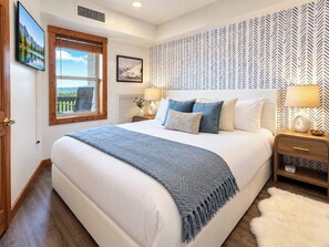 A bedroom with a large bed, a window with a view, a patterned wall, and a nightstand with a lamp. - Highland House 317 Ski In Out Village Hot Tub Wifi (Snowshoe)