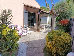 Eine Terrasse mit Sitzgelegenheiten im Freien, ein Glastür-Eingang und ein kleiner Garten mit verschiedenen Pflanzen.