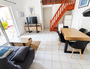 Ein moderner Wohnraum mit einer Couch, einem Holzesstisch, einem Fernseher und einer Treppe.