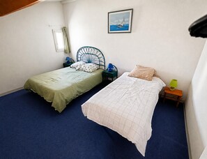Ein Zimmer mit zwei Betten, einem gerahmten Bild an der Wand und einem kleinen Tisch mit einer Lampe.