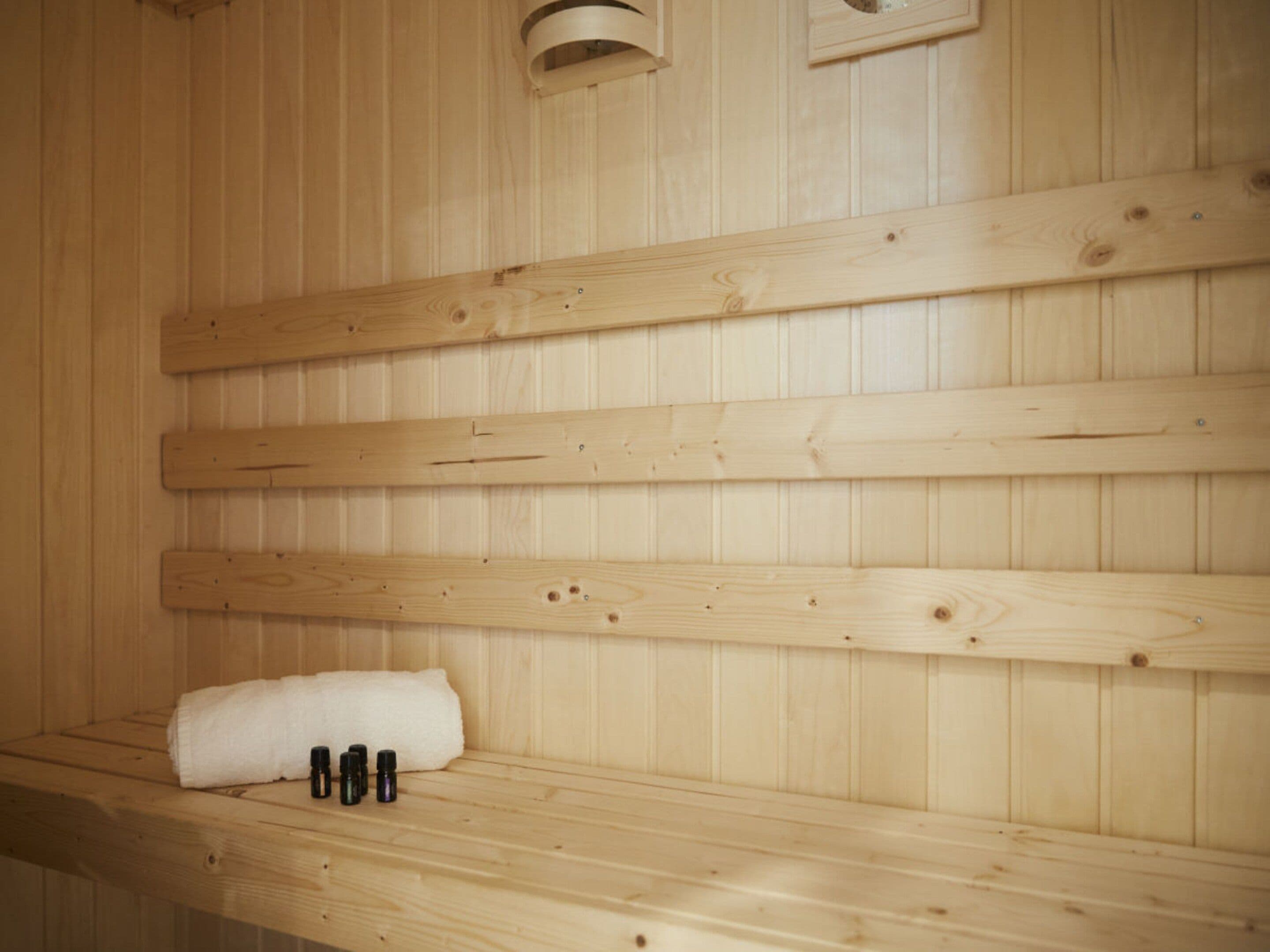Een houten sauna met banken en een plankje waarop een handdoek en flesjes staan.