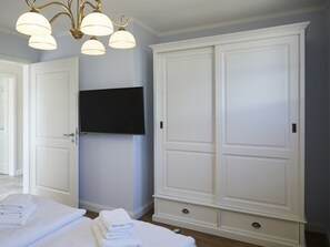 Ein Hotelzimmer mit großem Kleiderschrank, einem wandmontierten Flachbildfernseher und einem Bett mit ordentlich gefalteten weißen Handtüchern.