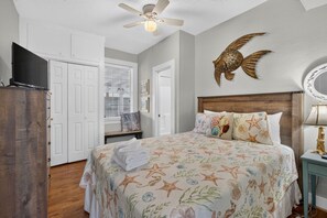 Ein Schlafzimmer mit einem Bett, einem Deckenventilator, einer an der Wand befestigten Fischdekoration und einem Fernseher auf einem Standfuß.