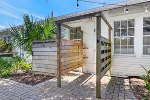En träport leder in till ett takförsett utomhusområde, med ett hus synligt i bakgrunden.