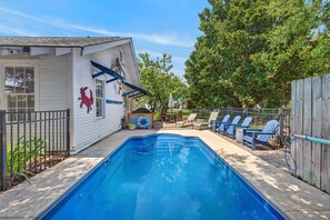 Ein wohnlicher Garten mit Swimmingpool, überdachter Terrasse und Holzzaun.