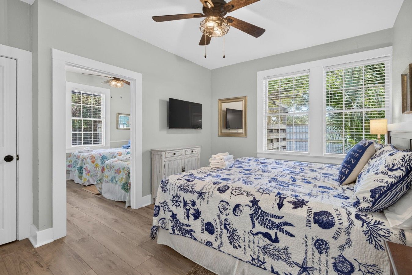 A bedroom with a bed, a ceiling fan, a TV, and a window with blinds.