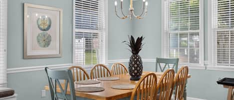 A dining room with a wooden table, chairs, a chandelier, and artwork on the wall.