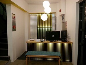 A reception desk with a computer, a telephone, and a bench in front. - Myeongdong Guesthouse Como (Seoul)