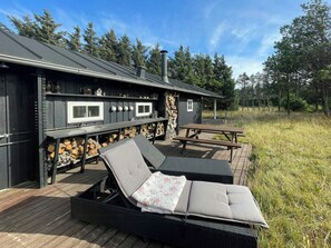 A wooden deck with two lounge chairs, a picnic table, and a stone wall with firewood. - Holiday home at Rubjerg Knude Fyr (Løkken)