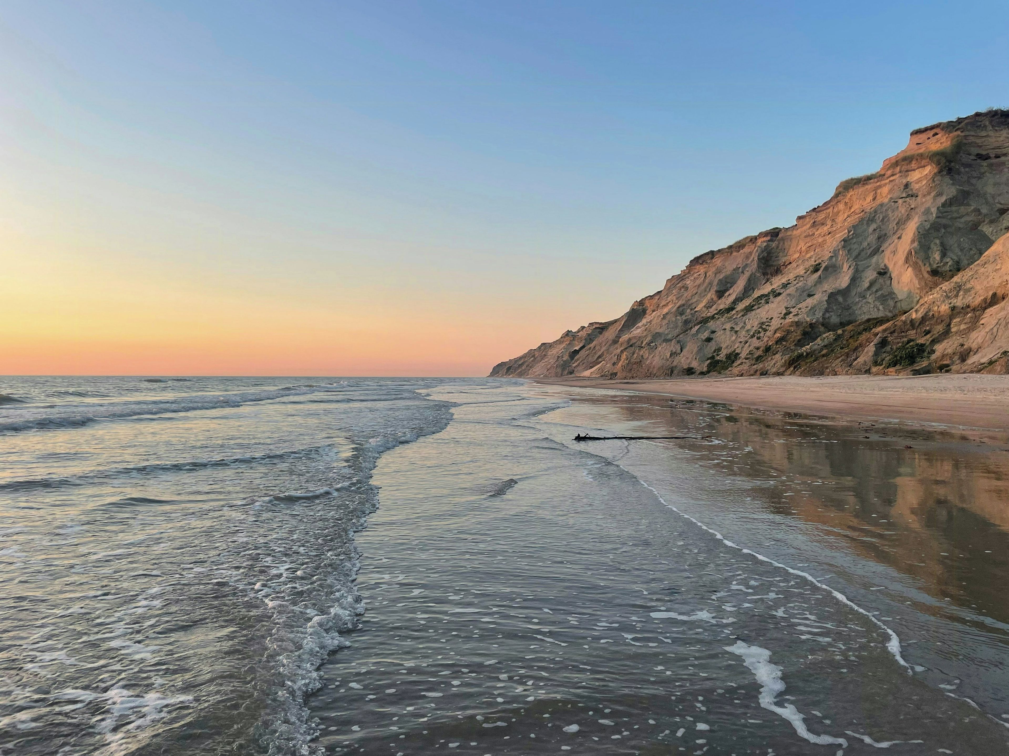 A beach with a rocky cliff and waves gently lapping at the shore.