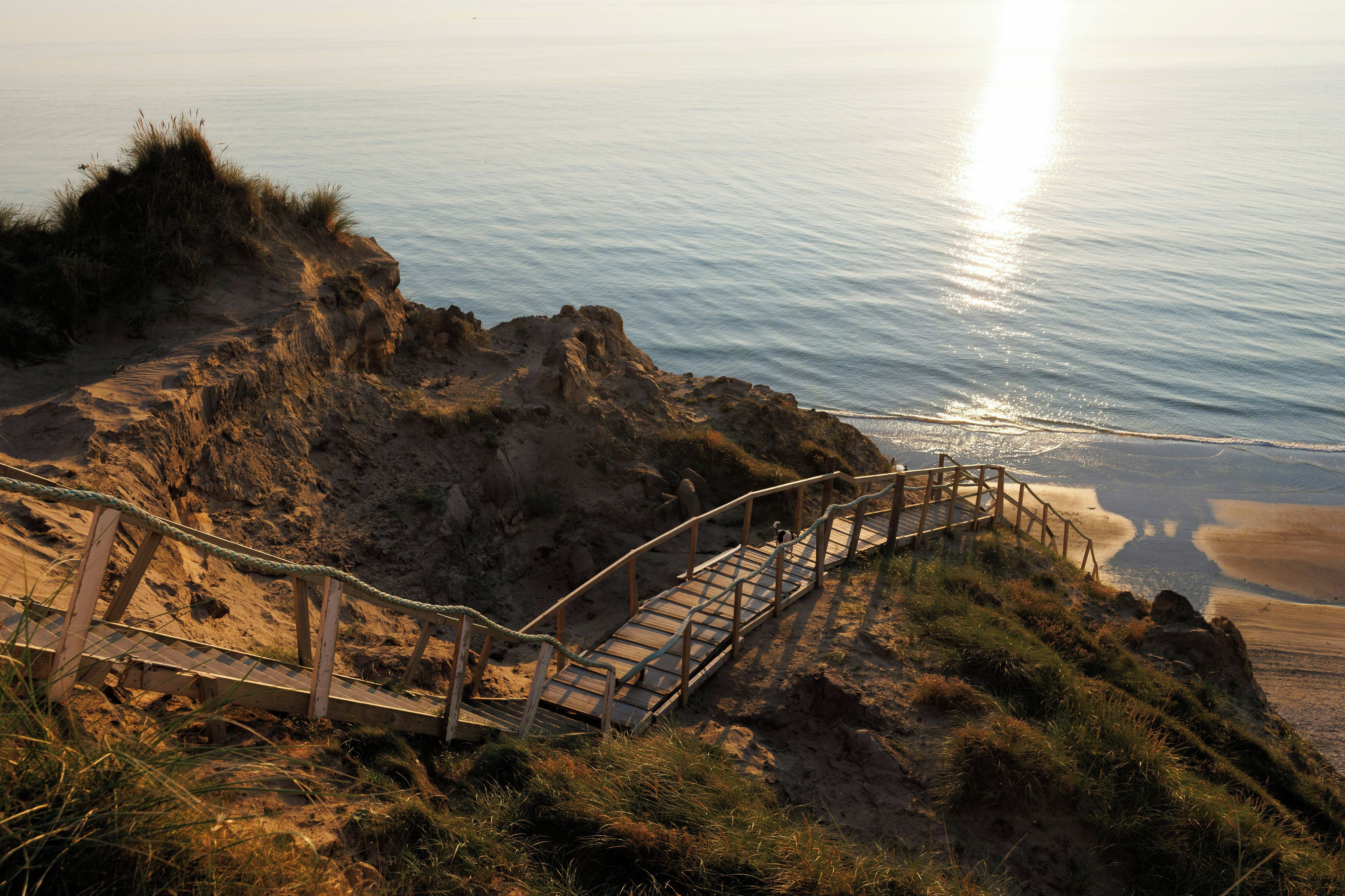 A wooden staircase leading down to a beach, surrounded by rocky terrain and sparse vegetation.