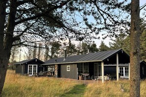 A row of cabins with a covered porch area, surrounded by tall trees and grassy fields. - Holiday home at Rubjerg Knude Fyr (Løkken)
