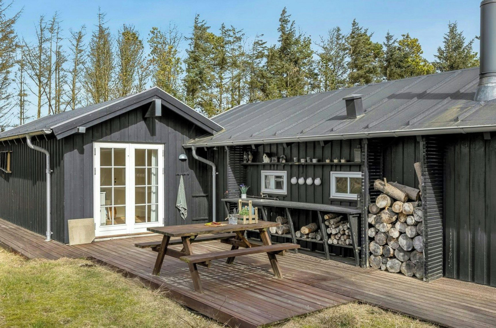 Una cabaña rústica con terraza de madera, mesa de picnic y chimenea.
