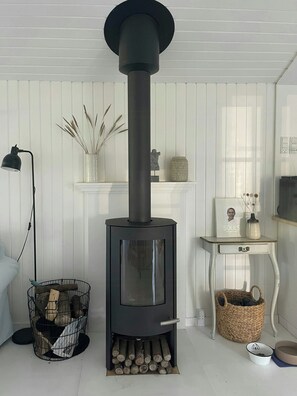 A modern living room with a black wood-burning stove, a floor lamp, and a basket with logs. - Holiday home at Rubjerg Knude Fyr (Løkken)