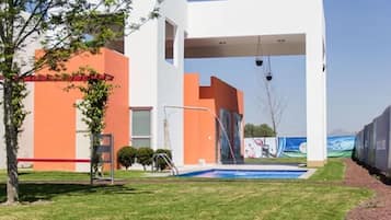 Un edificio moderno con piscina, zona cubierta y una barrera roja.