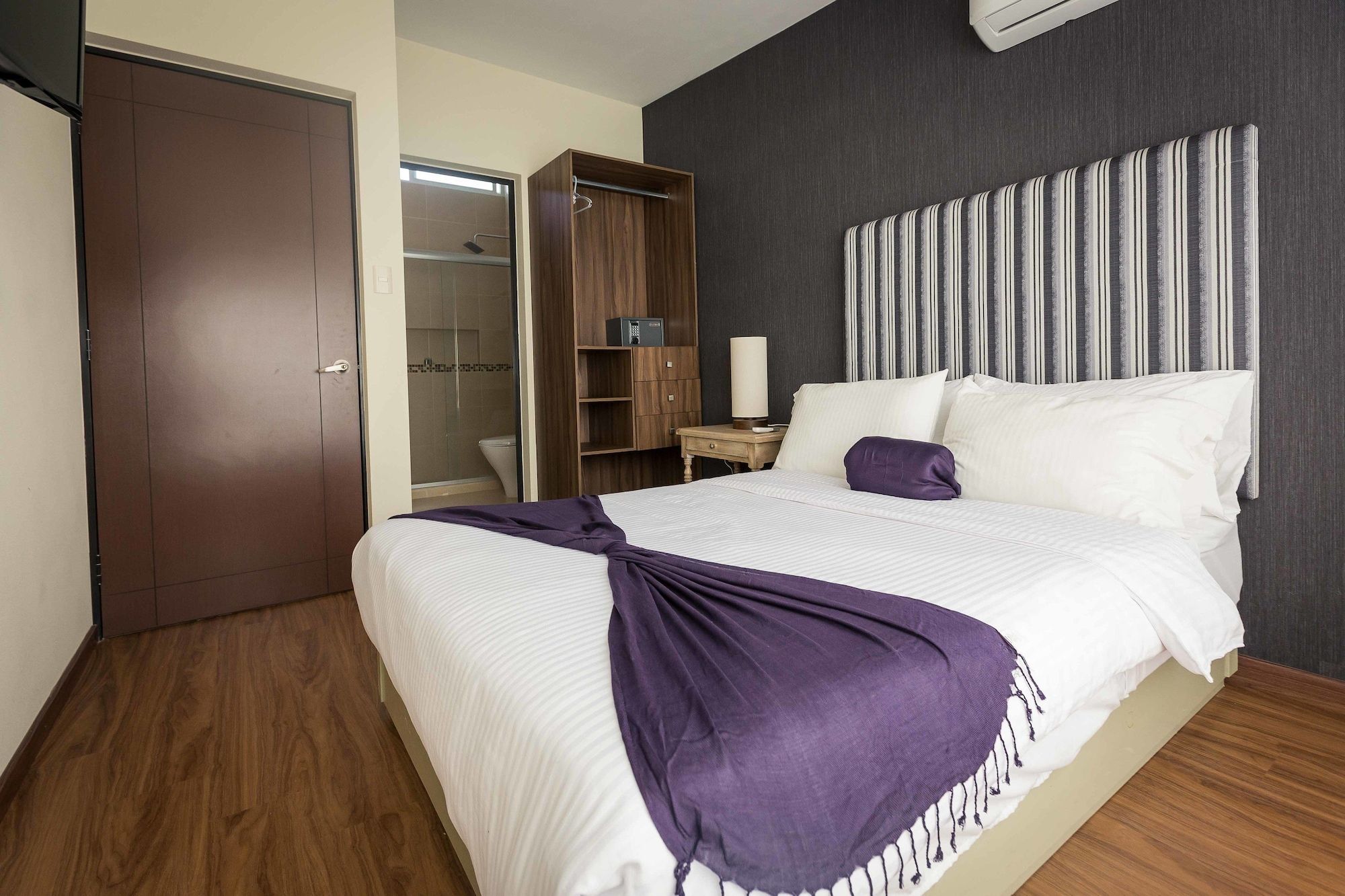 Habitación de hotel con cama, mesita de noche, lámpara, armario y baño con ducha e inodoro.