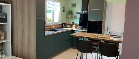 A modern kitchen with a wooden countertop, a sink, and a stove. There are two bar stools and a dining table.