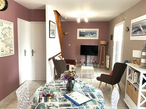 Ein Wohnzimmer mit Fernseher, einem Esstisch mit Tischdecke im Seglerstil und einem Bücherregal.