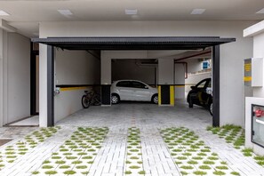 A covered parking area with a white car and a bicycle. - 3-bedroom apartment, 150m from Perequê beach, 1 parking space, near the lake and pier, Hard Rock Cafe. (Porto Belo)