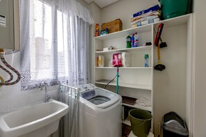 A laundry area with a washing machine, a sink, and shelves with cleaning supplies. - 3-bedroom apartment, 150m from Perequê beach, 1 parking space, near the lake and pier, Hard Rock Cafe. (Porto Belo)