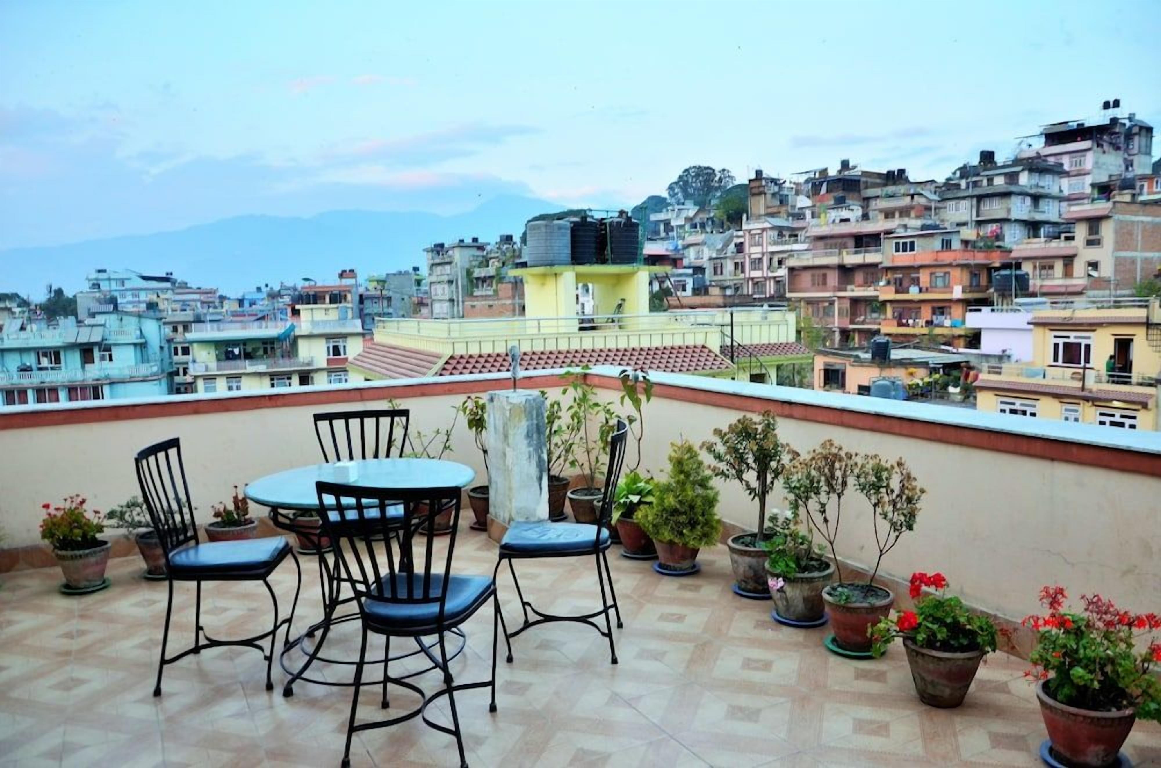 A rooftop terrace with a table and chairs, potted plants, and a view of a densely packed cityscape.