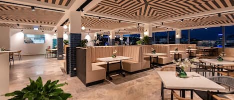 A modern indoor space with seating areas, tables, and a view through large windows.