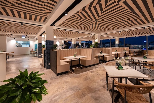 A modern indoor space with seating areas, tables, and a view through large windows. - Harbor Hotel and Casino Curacao (Willemstad)