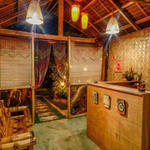 Un mostrador de recepción de madera con un panel de pared tejido, una lámpara colgante y una planta pequeña en la barra.