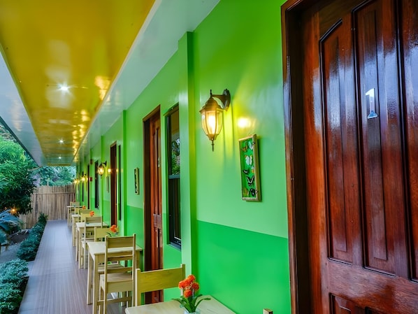 A covered outdoor area with a row of wooden doors, a pathway, and tables with chairs. - Butterfly Totem Guesthouse (Puerto Princesa)